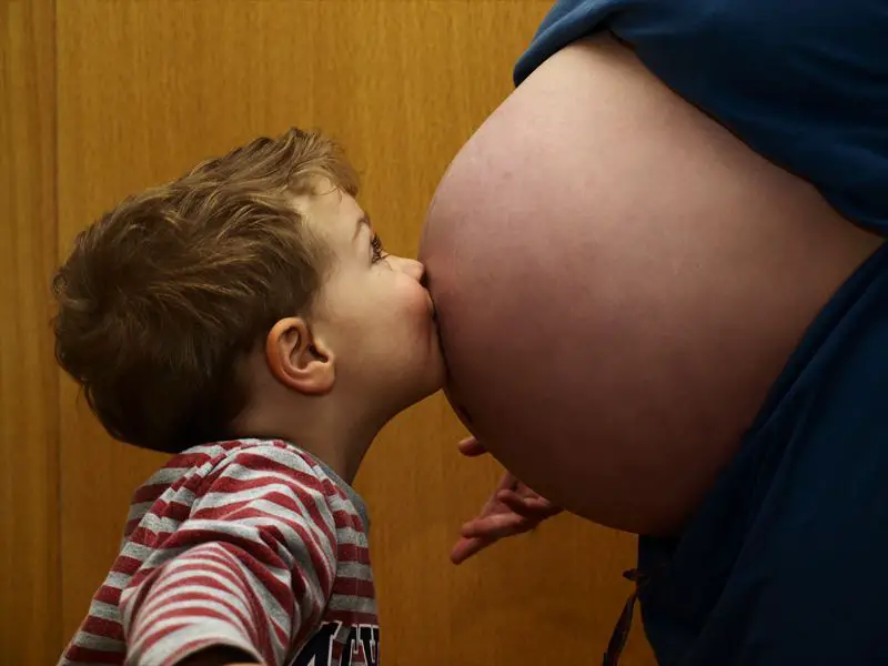 child kissing pregnant belly